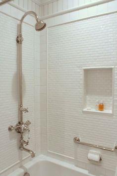 a white tiled bathroom with a tub and shower head