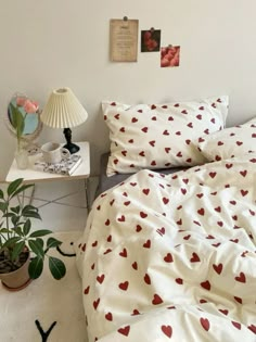 a bed with white sheets and red hearts on it, next to a small table