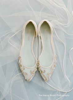 white wedding shoes with beading and pearls on the bottom are laying on a light blue background