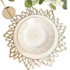 a white and gold plate sitting on top of a table next to a vase with flowers