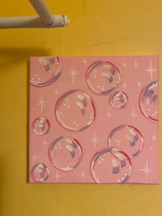 a pink painting with bubbles on it sitting on a yellow wall next to a white pipe