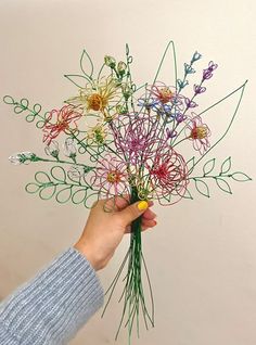 a person holding a bunch of flowers made out of string and paper with scissors in their hand