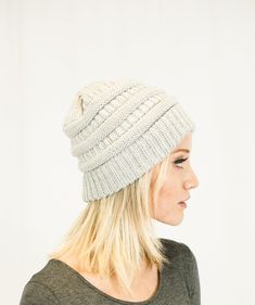 a woman with blonde hair wearing a white knitted beanie and looking off to the side