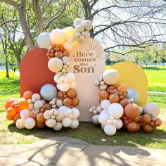 there is a sign with balloons on it in the grass next to some trees and bushes