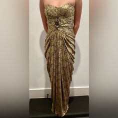 a woman in a gold dress standing against a wall with her hands on her hips