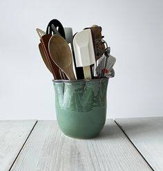 a cup filled with utensils sitting on top of a wooden table next to a white wall