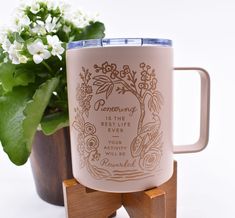 a coffee mug sitting on top of a wooden stand next to a potted plant