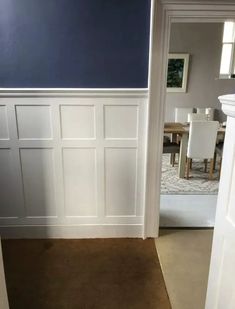 an open door leading to a dining room with blue walls and white wainscoting