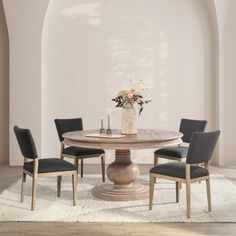 a round dining table with four chairs around it and a vase on the table top