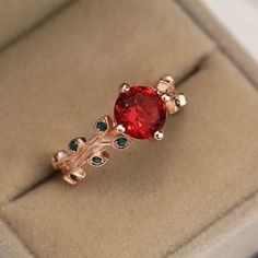 a close up of a ring in a box with a red stone and green stones