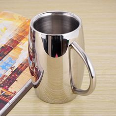 a stainless steel coffee mug sitting on top of a wooden table next to a book