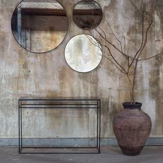 three round mirrors hanging on the wall above a bench and vase with tree branches in it