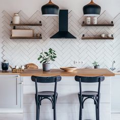 two stools sit at the counter in front of a white tiled wall and shelves