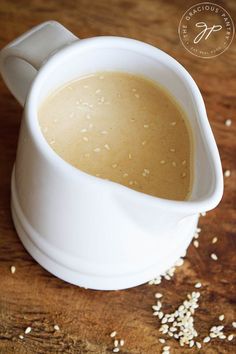 a white pitcher filled with liquid sitting on top of a wooden table next to sesame seeds