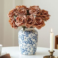 a blue and white vase filled with pink roses on top of a table next to a lit candle