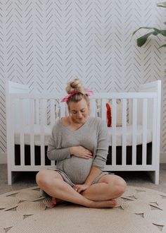 a pregnant woman is sitting on the floor in front of her crib and holding her stomach