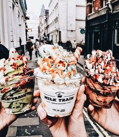 three ice cream sundaes with sprinkles and toppings in their hands