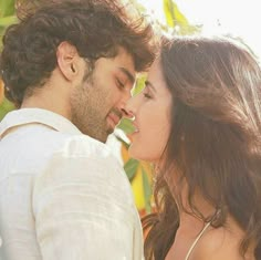 a man and woman kissing each other in front of green leaves on a sunny day