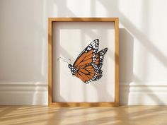 an orange and white butterfly is in a wooden frame on the floor next to a wall