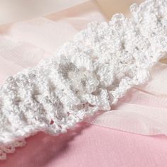 a close up of a white crocheted headband on a pink fabric material