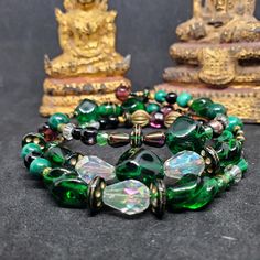 "The Caribou bracelet is named after the color of the trees in Caribou Wilderness area, a favorite childhood haunt. It features antique and vintage glass, gemstone and brass beads: 1980s old stock malachite, early 1900s green glass nailheads, West German emerald faceted nuggets, Venetian-style transparent green oval beads with gold aventurine, Italian green-lavender foil seed beads, 18th century French brass \"torse\" beads and many more." Green Jewelry With 108 Beads For Festival, Traditional Green Beaded Bracelets For Festival, Green Beaded Bangle Bracelets For Festival, Handmade Malachite Spiritual Beaded Bracelets, Handmade Malachite Beaded Bracelets For Spiritual Use, Green Spiritual Beads For Healing, Spiritual Healing Glass Bracelets, Green Bead Bracelet For Festivals, Green Hand Wrapped Beaded Bracelets