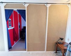 a room with three doors and a desk in the corner, behind which there is a curtain