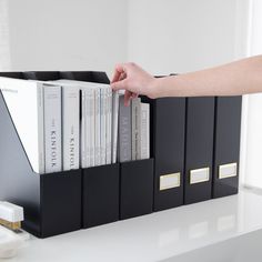 a person is reaching for books in a black book case on a white table with gold trim