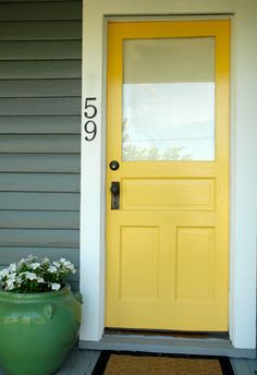 a yellow front door on a house with white flowers in the pot next to it