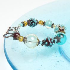 "This Turquoise floral lampwork boho bracelet is a perfect gift for women! This glass is rather durable as it is put in a very high temperature after the bead is made. This lampwork bracelet fits a 15.5-16.5cm (6.1\"-6.5\" inch) diameter wrist. If you need bigger or smaller size bracelet, please, write me the diameter of your wrist when making an order. Dimentions: 21cm. Materials: artist lampwork beads, metal and glass beads, metal fittings. Colors used: teal, turquoise, chocolate brown. Please Bohemian Turquoise Bracelets With Spacer Beads, Bohemian Czech Glass Bracelets With Spacer Beads, Turquoise Czech Glass Bracelets With Large Beads, Bohemian Charm Bracelet With Spacer Beads, Handmade Beaded Bracelets With Czech Glass, Czech Glass Bracelet Jewelry, Turquoise Czech Glass Bracelets With Colorful Beads, Turquoise Bracelets With Large Beads For Gifts, Turquoise Czech Glass Bracelet For Gift