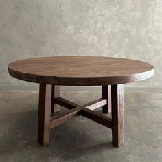 a round wooden table sitting on top of a cement floor next to a gray wall