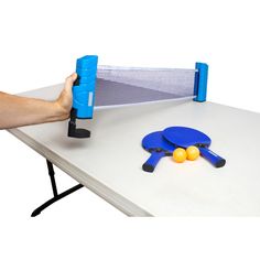 a ping pong table with two paddles and three balls on it, being held by a hand