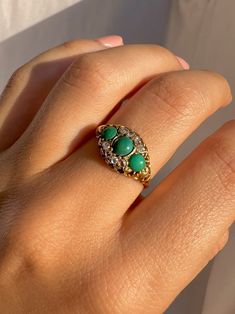 a woman's hand with a green ring on top of her finger and an emerald stone in the middle