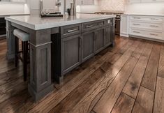 a large kitchen with white cabinets and wood flooring on one side and an island in the other