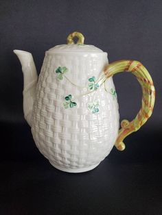 a white ceramic tea pot with green and yellow designs on the handle, sitting on a black surface