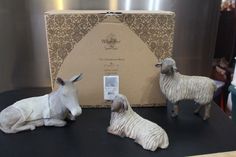 three ceramic sheep sitting on top of a table next to a box with a label