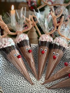 four cones with candy in them decorated like reindeer noses and antlers on a polka dot table cloth