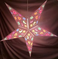 a lighted star hanging from the ceiling in front of a black backdrop with stars and moon designs