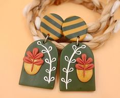 two green and yellow earrings with red flowers on them sitting next to a rope bracelet