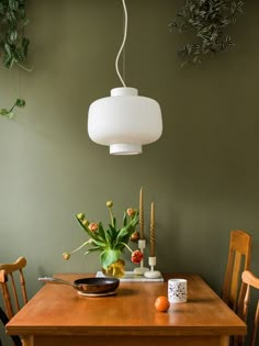 a wooden table topped with a bowl of fruit next to a light hanging over it