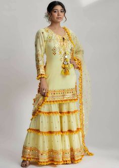 The mahika layered sharara set with mirror work, pompoms and tassels, along with detailed hand and machine embroidery, is a masterpiece of craftsmanship and style. It is the perfect choice for those seeking an elegant and exquisite outfit for special occasions, weddings, or cultural celebrations. Luxury Unstitched Sharara With Meenakari Details, Luxury Designer Sharara With Meenakari, Luxury Sharara With Motifs For Navratri, Luxury Meenakari Sharara For Traditional Ceremonies, Luxury Meenakari Sharara For Wedding, Luxury Yellow Sharara With Dupatta, Luxury Tiered Sharara For Navratri, Luxury Yellow Sharara With Self Design, Luxury Long Sharara For Navratri