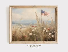 an american flag hangs on the wall above a painting of wildflowers and grasses