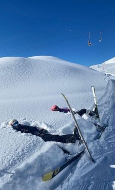 two skiers laying down in the snow with their skis propped up against them