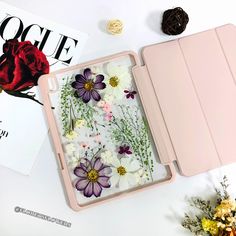 an open pink case with flowers on it next to a magazine and some dried flowers