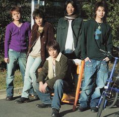 four young men standing next to each other in front of a blue bicycle and bench