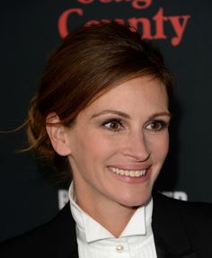 a woman in a suit and white shirt smiling at the camera with her hair pulled back