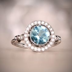 A platinum halo ring that features a round cut natural aquamarine weighing approximately 1 carat. Surrounding the center gemstone is a row of old European cut diamonds. This ring has a low profile and has a detailed under-gallery. The measurements of this ring including the halo are 12.50mm. The measurements of the center aquamarine are 7.50mmm. Blue Topaz Platinum Ring With Halo Setting, Light Blue Aquamarine Rings With Halo Setting, Blue Topaz Halo Ring For Wedding, Aquamarine Diamond Ring With Halo Setting For Formal Events, Light Blue Topaz Ring With Diamond Halo Setting, Light Blue Topaz Halo Ring With Diamonds, Anniversary Aquamarine Diamond Ring With Halo Setting, White Gold Aquamarine Diamond Ring, Aquamarine Diamond Ring With Halo Setting