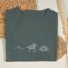 Get ready for summer with our Turtle Embroidered Beach Shirt, a must-have for beach lovers and ocean enthusiasts. Design: This summer shirt features an intricate embroidery of a charming turtle, waves, and a radiant sun. The detailed turtle embroidery and sun design capture the essence of beach life, making it a standout piece for any beach bum. Material: Crafted from high-quality fabric, our beach shirt offers both comfort and durability. Its soft, breathable material ensures you stay cool and Beach Embroidered Short Sleeve T-shirt, Embroidered Short Sleeve Beach T-shirt, Green Surfing T-shirt For Summer, Embroidered Short Sleeve T-shirt For Beach, Embroidered Cotton T-shirt For Beach, Beach Cotton Tops For Surfing, Embroidery Designs For T Shirts, Simple Tshirt Design Ideas, Embroidery On A Shirt