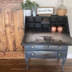 an old desk has been painted black and is next to a wooden cabinet with potted plants on it