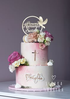 a wedding cake with flowers and a cross on the top is decorated in pink, white and gold