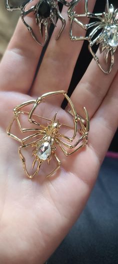 a person's hand holding three gold spider brooches